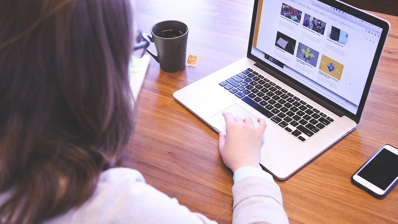 Ảnh chụp một người ngồi làm việc với laptop trên bàn gỗ, cạnh tách cà phê và điện thoại