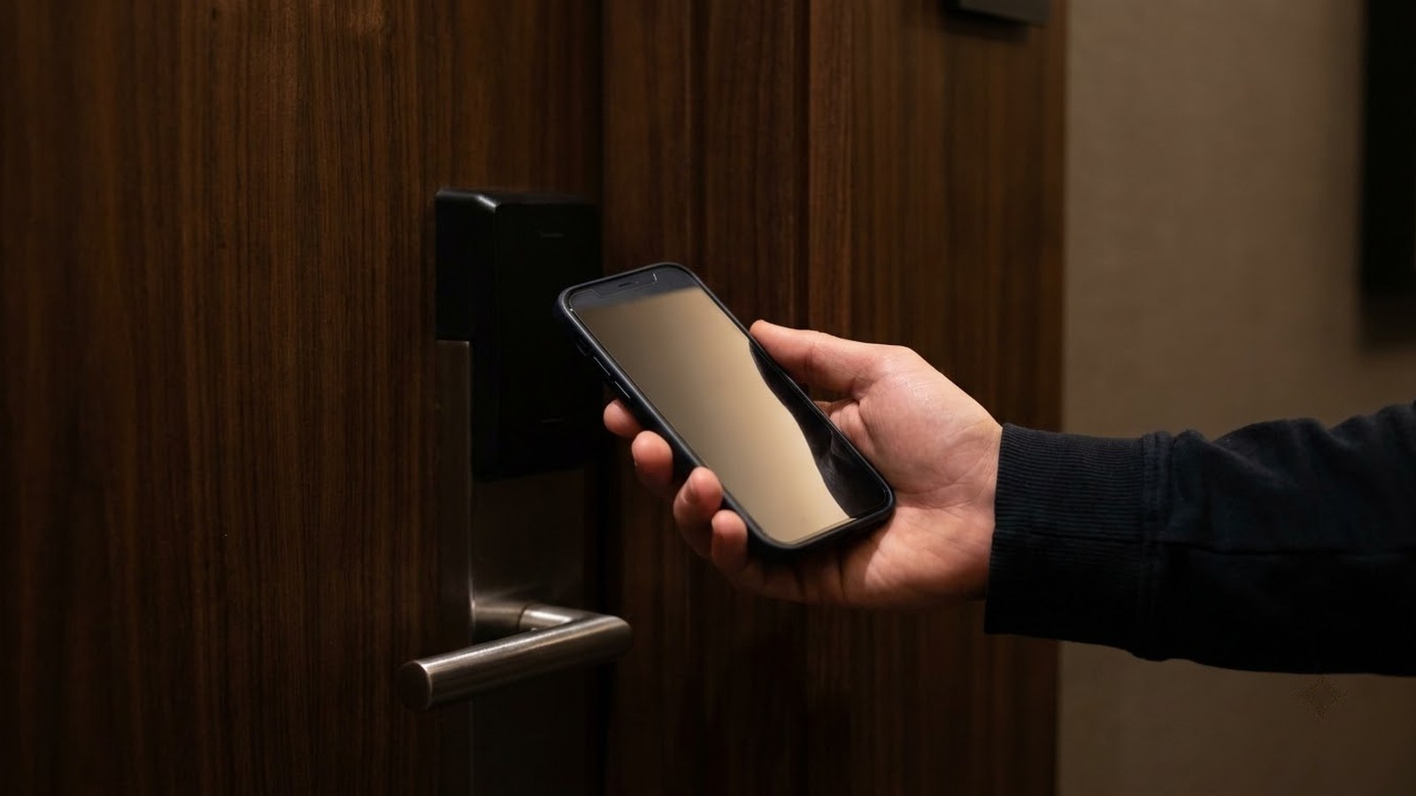 A hand holding a phone up to an electronic lock on a hotel room door