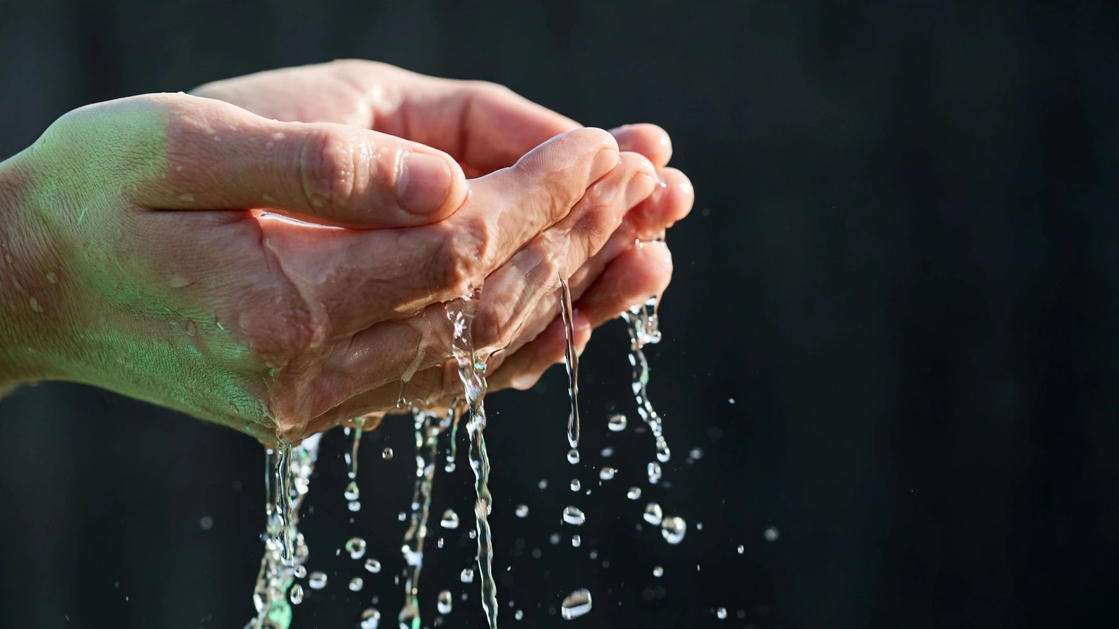 Two cupped hands holding water with thin streams and droplets escaping between the fingers